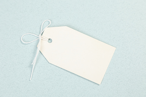 An empty white price tag lies on a gray-blue background with a soft shadow.
