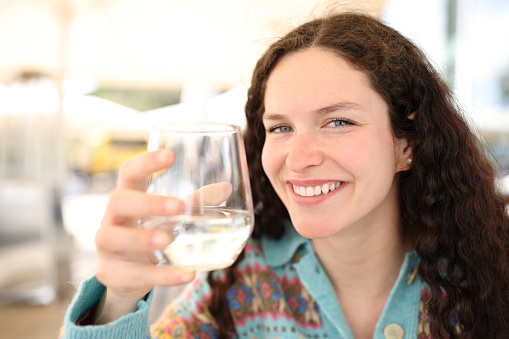 Happy woman holding water glass in a bar looks at you