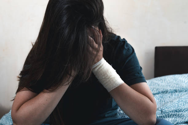 Young unhappy woman with a bandage on her hand hides her face. Depressed female scared and stressed suffering from depression and anxiety. stock photo