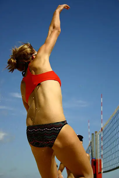 Female Beach Volleyball player spiking ball over net with sky blue background.