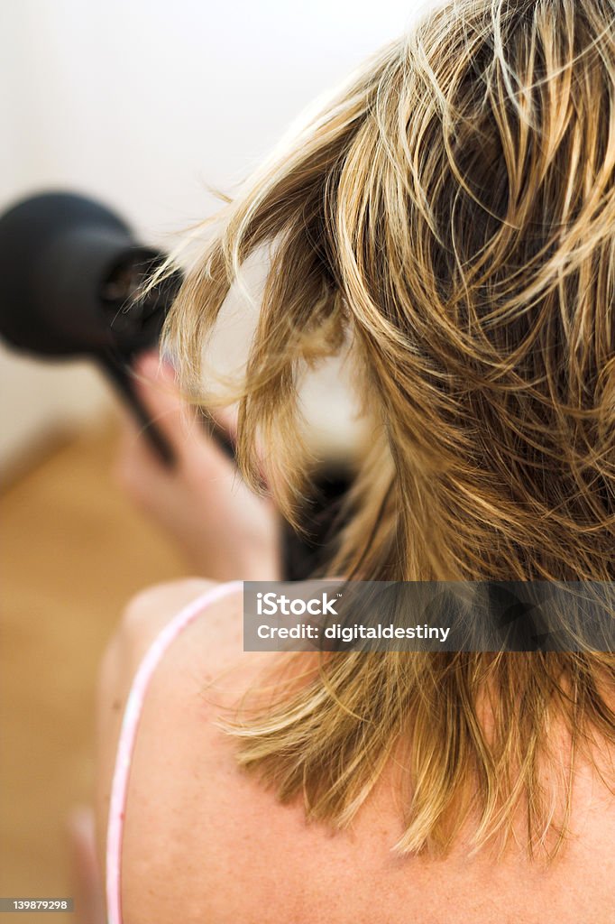 woman drying hair with a hairdryer A lady dries her shoulder length wet blonde hair with an electric hairdryer Adult Stock Photo