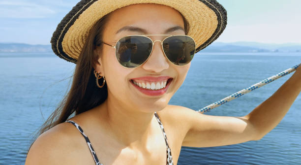 Woman standing on sailboat Portrait of young woman wearing sun hat while standing on boat deck during sunny day. hoop earring stock pictures, royalty-free photos & images