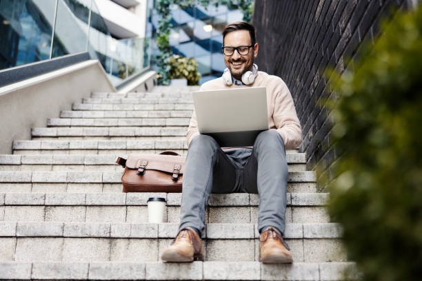 istock A happy man sits on the stairs outside and using laptop. 1398799361