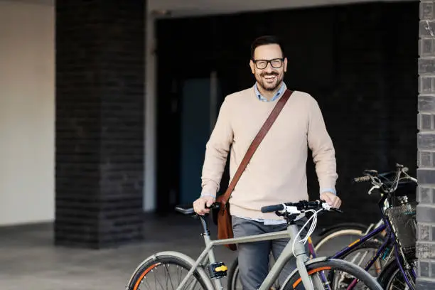 Photo of A happy man standing on public place and posing with bicycle.