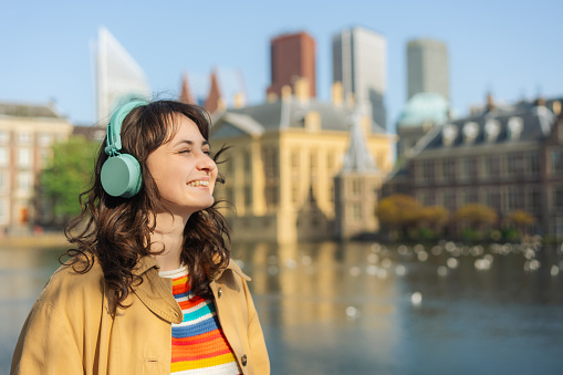 Young Caucasian woman in coat   listening to music in headphones in The Hague