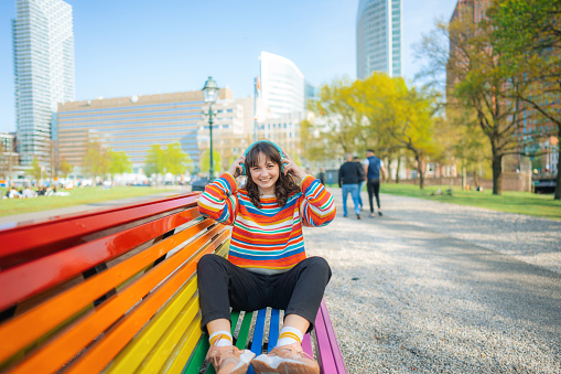 Young Caucasian woman  listening to music in headphones on rainbow coloured bench