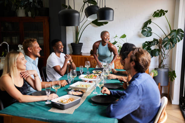 lachende junge frau, die eine dinnerparty für eine gruppe von freunden veranstaltet - feast day fotos stock-fotos und bilder