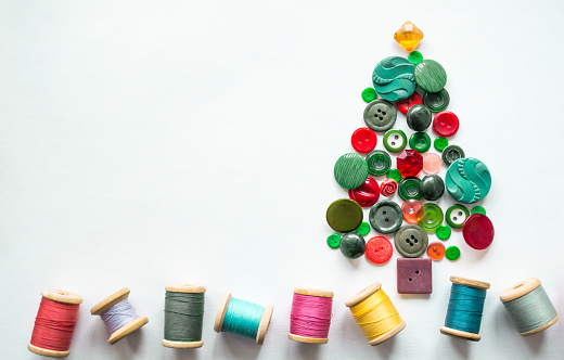 Tree made of buttons green, red color. Multicolored threads with wooden spools. White background, copy space. Creative Christmas concept.