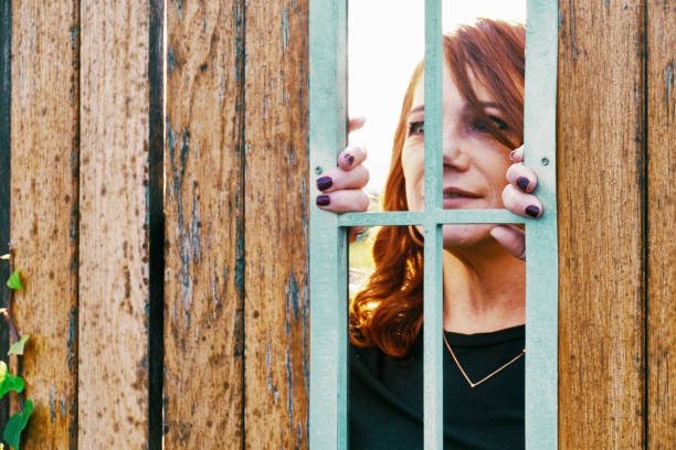 A white woman peeks through a wooden fence
