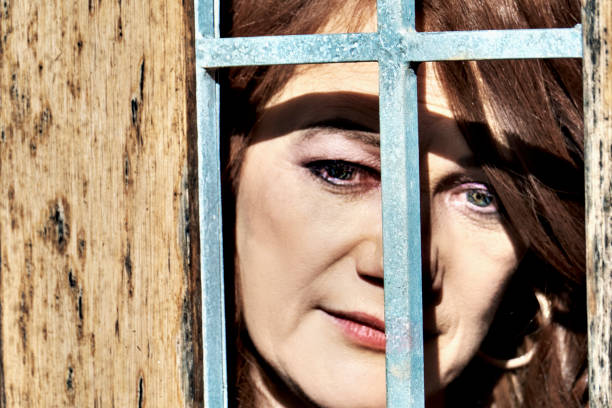 A white woman peeks through a wooden fence