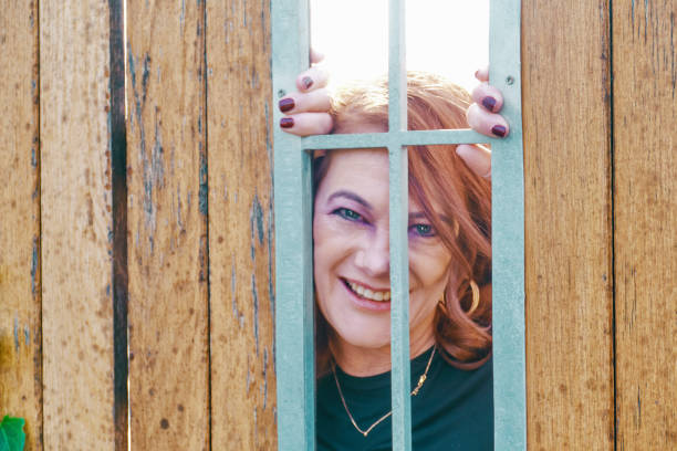 A white woman peeks through a wooden fence