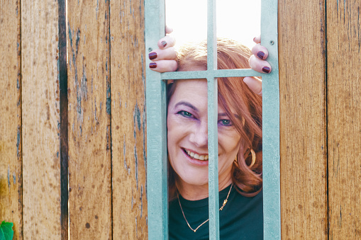 A white woman peeks through a wooden fence