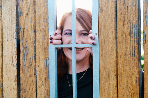 A white woman peeks through a wooden fence