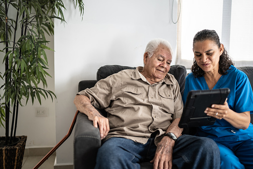 Home Caregiver showing tablet to senior man at his house