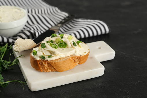 Delicious sandwich with cream cheese and microgreens on black table