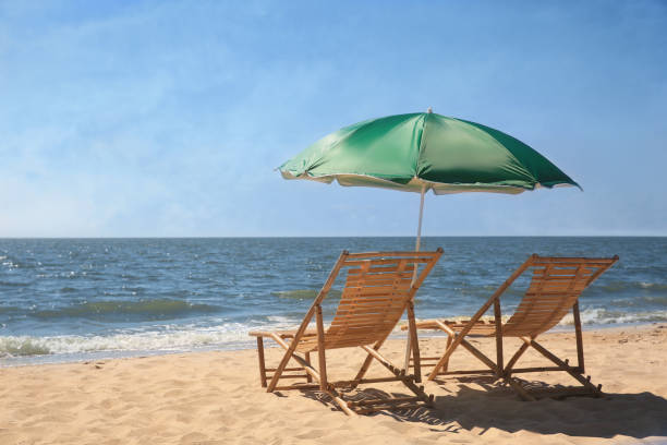 istock Green beach umbrella and deck chairs on sandy seashore 1398805257