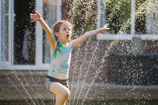 A happy girl is jumping through a sprinkler