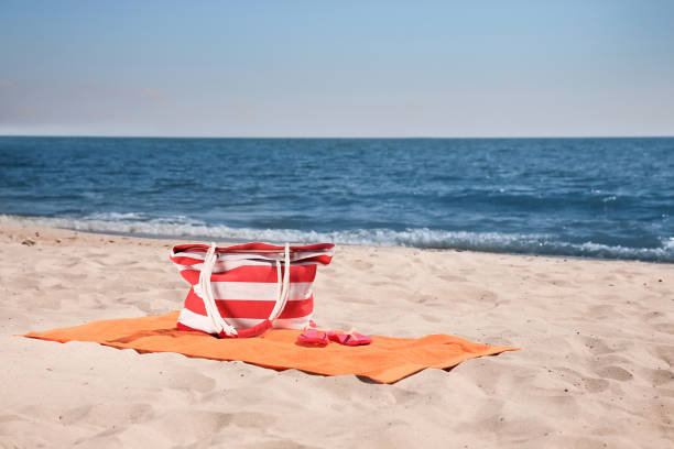 istock Soft orange beach towel, bag and flip flops on sandy seashore 1398805559