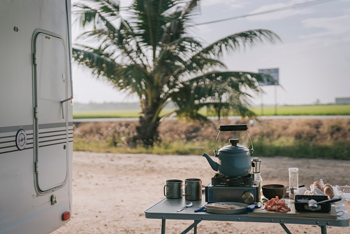 boiling kettle on camping stove beside campervan parked beside paddy field in the morning