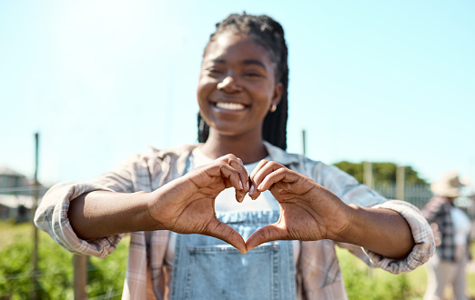 Portrait of a happy farmer. Young farmer creating a heart shape with her hands. African american farmer showing love. Farmer standing in her garden. Farmer making a gesture with her hands