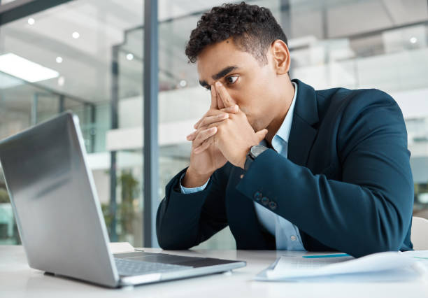 istock Young mixed race businessman looking stressed while working on a laptop alone at work. Hispanic businessperson looking worried working at a desk in an office 1398809584