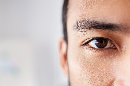 Closeup portrait of a handsome young mixed race man standing at work in an office job. Young hispanic male with naturally long eyelashes and neat eyebrows showing his healthy brown eye