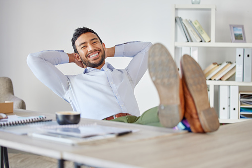 Portrait of mixed race business man relaxing with his feet up at his desk. Boss looking comfortable and satisfied at workplace. Business success