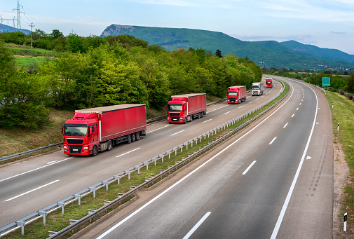 Series of red Trucks and one white truck on highway, cargo transportation concept in springtime - freight service