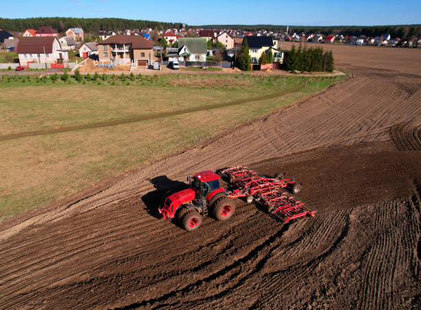 Tractor disk harrow on ploughing a soil. Sowing seed on plowed field on sunset. Seeding in agriculture.