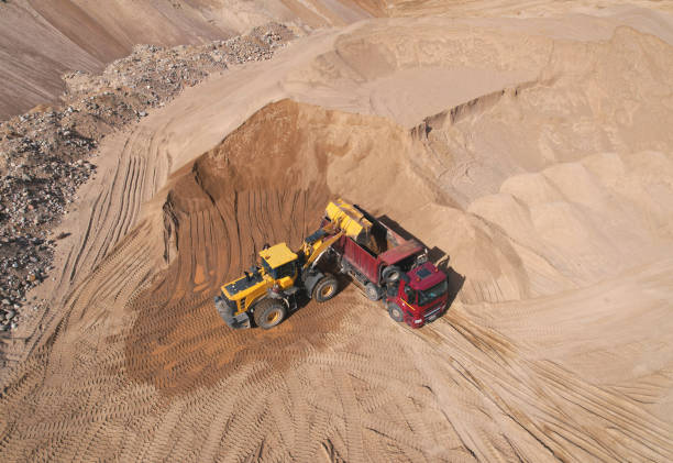 Front end loader on earthworks in quarry. Wheel loader load sand in dump truck in open pit. Heavy machinery on developing opencast. Mining truck transports sand from open-pit mining, aerial view.