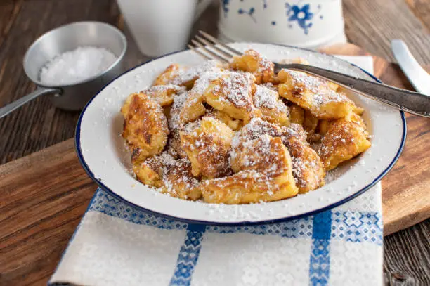 Homemade fresh cooked traditional Kaiserschmarrn with powdered sugar topping. Served on a old fashioned enamel plate on rustic and wooden table background