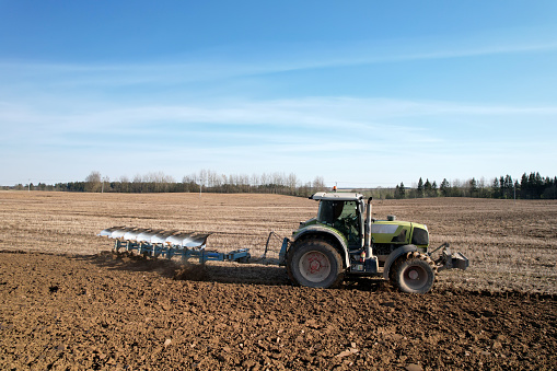 Tractor with plow on soil cultivating. Green tractor plowing field, drone view. Cultivated land and soil tillage. Agricultural tractor on field cultivation. Tractor disk harrow on plowing farm field.