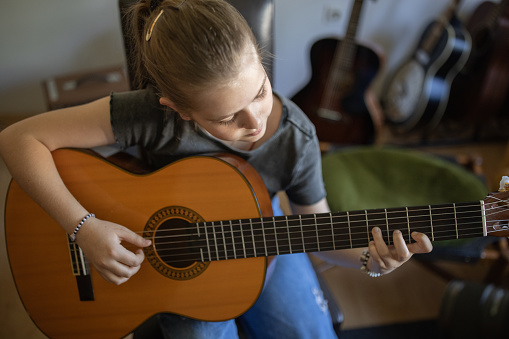 High angle view of young Caucasian girl playing acoustic guitar at the music school