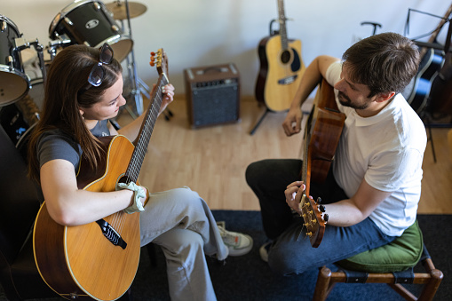 Caucasian male music teacher, playing acoustic guitar, while leading a class with female student