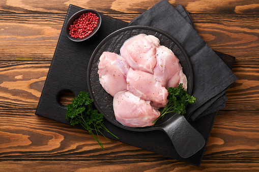 Raw chicken thigh fillet without skin with herbs and spices on old wooden background. Farm poultry meat. Top view with copy space. Mock up.
