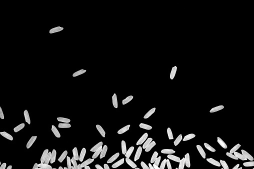 A pile of raw white rice is floating on a black background.