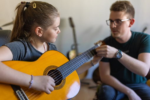 Caucasian male music teacher, teaching girl how to play guitar