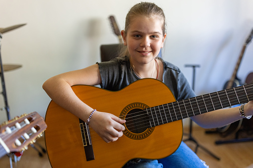 Portrait of young Caucasian girl playing acoustic guitar at the music school