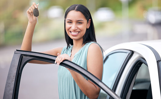Portrait of a cheerful mixed race woman holding keys to her new car. Hispanic woman looking happy buying her first car or passing her drivers test. Hispanic woman smiling against bright copyspace