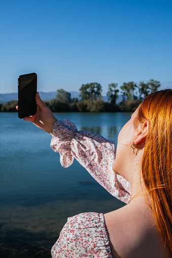 Red-haired girl taking a selfie with the river in the background