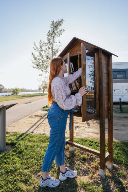 red-haired girl taking a book from a public bookstore outdoors