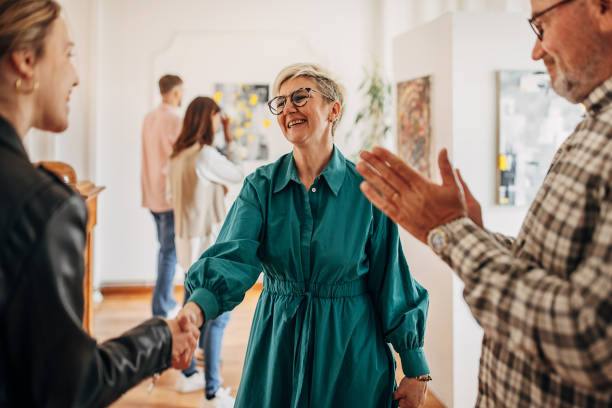 People in art gallery Diverse group of visitors in modern art gallery having shaking hands with female artist. gallery opening stock pictures, royalty-free photos & images