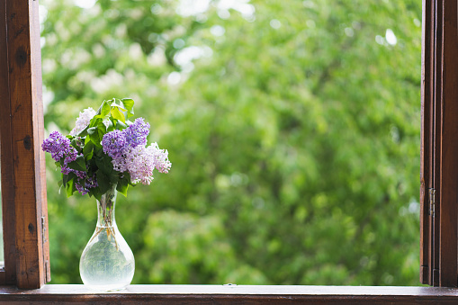 Vase with spring flowers lilac on a wooden window. Cozy spring concept