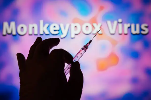 A hand holding a medical syringe with the word Monkeypox in the background. Is a viral disease that occurs mainly in central and western Africa. It's called monkeypox.