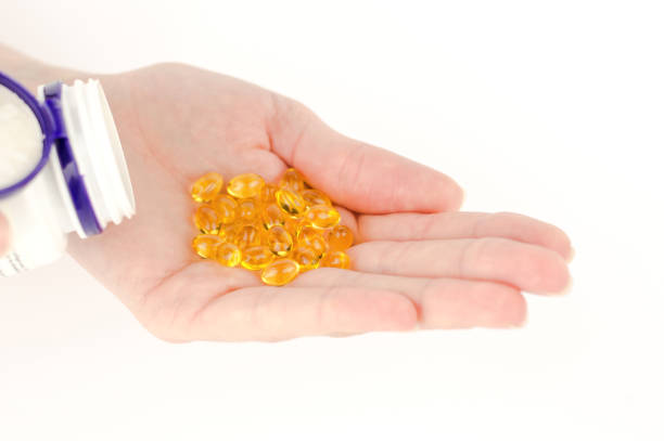 желтые таблетки в женской руке. витамин омега-3 в женской руке в капсулах. желтый рыбий жир капсулы - d3 стоковые фото и изображения