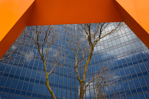 An orange arch frames the Frank J Lausche State Office Building in downtown Cleveland, Ohio.  A cloudy sky and the Terminal Tower are reflected in the glass.