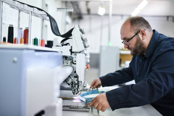 istock Bearded Male Worker In Textile Factory Using Colored Thread For Cloth Piece Sewing In Sewing Factory 1398829788