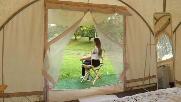 View from modern canvas tent on travel woman sitting on folding chair outside modern tent, relax and enjoy nature in wild safari park. Summer adventure, nature vacation, eco tourism, digital detox vista desde la moderna tienda de lona en la mujer de viaje sentada en una silla plegable fuera de la tienda moderna, relájese y disfrute de la naturaleza en el parque de safari salvaje. aventura de verano, vacaciones en la naturaleza, ecoturismo, desintox