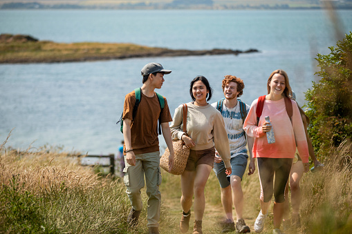 Wide angle shot of a group of mixed ethnic teens on a walk along the coastline together at Holy Island in the North East of England in summer.