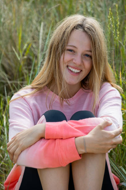 Young woman smiling at the camera while sitting in marram tall grass. She is at a beach at Holy Island in the North East of England in summer.